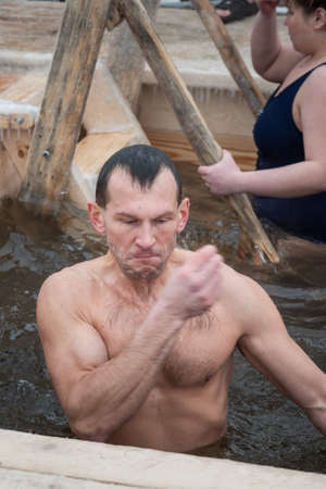 Nizhny Tagil, Russia - January 19, 2020: Man bathes into cold water of ice-hole on Epiphany day. Traditional ice swimming in Orthodox church Holy Epiphany Dayのeditorial素材