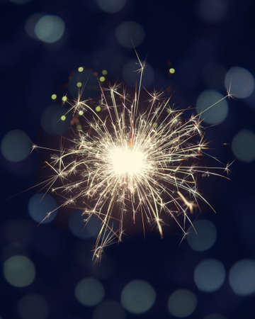 Glittering burning sparkler on dark background with bokeh lightsの写真素材
