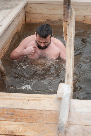 Nizhny Tagil, Russia - January 19, 2020: Man bathes into cold water of ice-hole on Epiphany day. Traditional ice swimming in Orthodox church Holy Epiphany Dayのeditorial素材