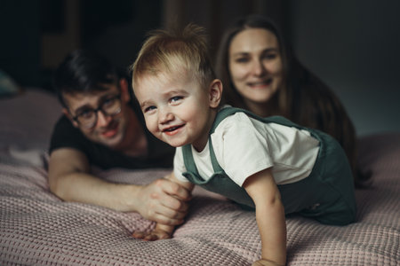 Happy family with little son lying and playing on bed at home. Soft focusの写真素材