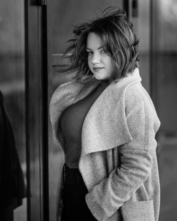 Brunette girl near wall on the street of city. Plus size model. Black and whiteの写真素材
