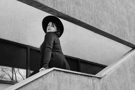 Brunette woman in hat on the stairs of building in city. Plus size model. Black and whiteの写真素材