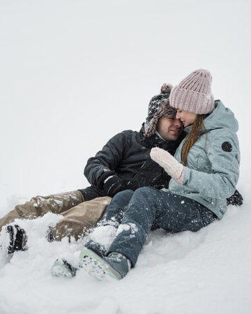 Loving guy and girl are lieing in the snow. Young happy couple walking in winter day