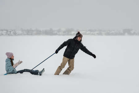 Man pulling snow tube with girlfriend. Young happy couple walking in the street in winter dayの写真素材