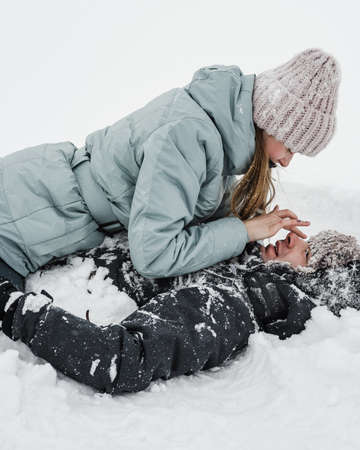 Loving guy and girl are lieing in the snow. Young happy couple walking in winter dayの写真素材