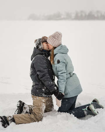Portrait of smiling couple in love are sitting in snow. Young happy couple walking in winter dayの写真素材