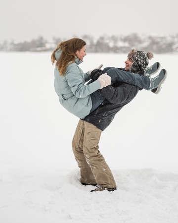 Young happy couple walking in winter day. Woman on man's shoulder by legsの写真素材