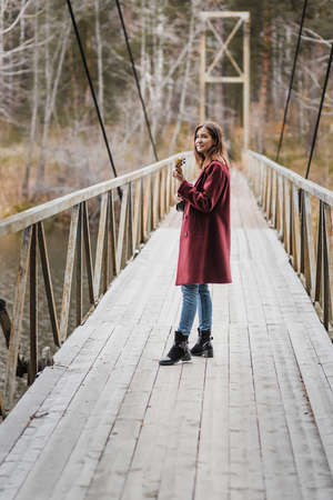 Young woman walking and playing ukulele guitar in bridge in autumn forestの写真素材