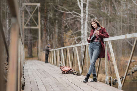 Young woman walking and playing ukulele guitar in bridge in autumn forestの写真素材