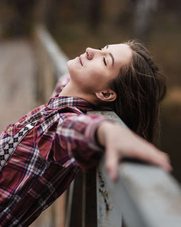 Young woman enjoys resting her head on fence in bridge on bridge in autumn forestの写真素材