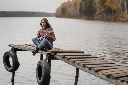 Young woman sitting and playing ukulele guitar on the wooden pier in autumn forestの写真素材