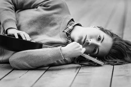 Portrait of young woman relaxing with ukulele guitar on the bridge in autumn forest. Black and white