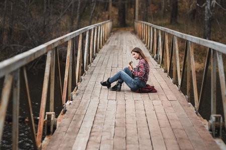 Young woman sitting and playing ukulele guitar on the bridge in autumn forestの写真素材