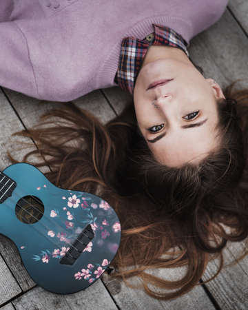 Portrait of young woman relaxing with ukulele guitar on the bridge in autumn forestの写真素材