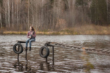 Young woman sitting and playing ukulele guitar on the wooden pier in autumn forestの写真素材