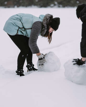 Couple of teenagers building snowman together in winter forestの写真素材