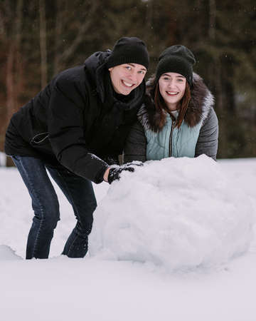 Couple of teenagers building snowman together in winter forestの写真素材