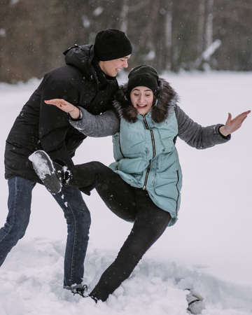 Happy couple teenagers having fun playing in snow in winter forestの写真素材