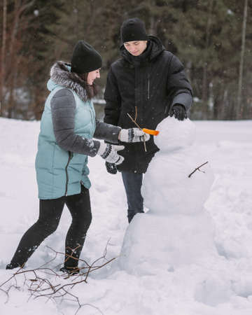 Couple of teenagers building snowman together in winter forestの写真素材