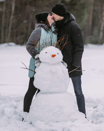 Couple of teenagers building snowman together in winter forestの写真素材