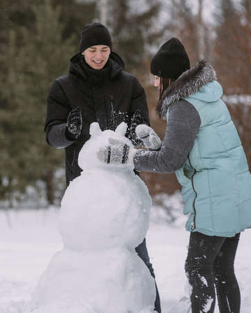 Couple of teenagers building snowman together in winter forestの写真素材