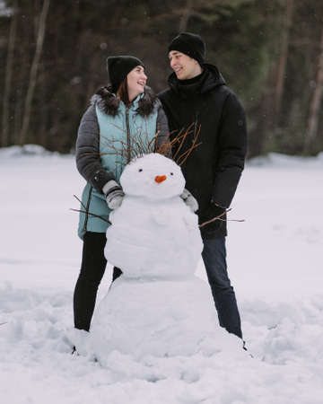 Couple of teenagers building snowman together in winter forestの写真素材