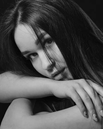 Studio portrait of pretty brunette woman lowering her head on hands on black background. Model looking at camera. Black and whiteの写真素材