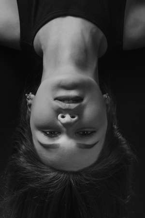 Studio portrait of pretty brunette woman upside down on black background. Model looking at camera. Black and whiteの写真素材