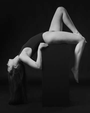 Pretty brunette woman in bodysuit posing on cube on black background. Black and whiteの写真素材