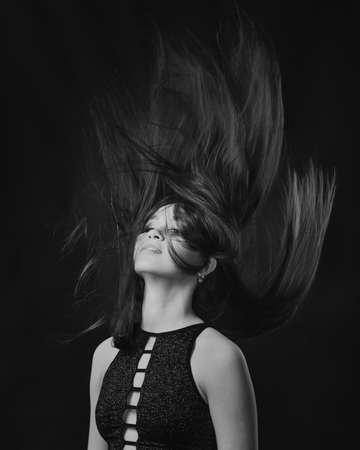 Studio portrait of pretty brunette woman with long hair flying on black background. Black and whiteの写真素材