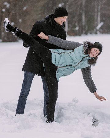 Happy couple of teenagers having fun playing in snow in winter forestの写真素材
