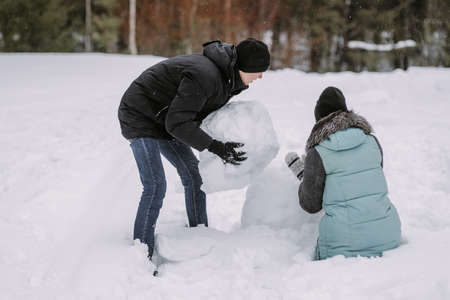 Couple of teenagers building snowman together in winter forestの写真素材