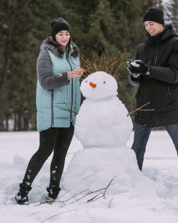 Couple of teenagers building snowman together in winter forestの写真素材