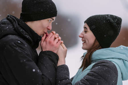 Portrait of couple of teenagers in winter forest. Boyfriend warming girlfriend's handsの写真素材