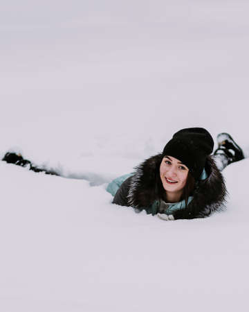 Beautiful young girl lying in the snow in winterの写真素材