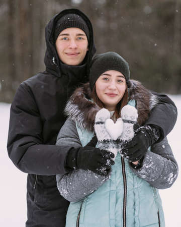 Portrait of couple of teenagers with snow heart in winter forestの写真素材