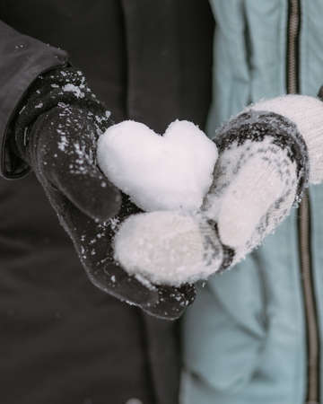 Hands of couple of teenagers with snow heart in winter forestの写真素材