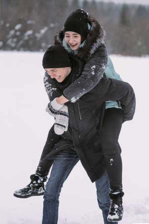 Happy couple of teenagers having fun playing in snow in winter forestの写真素材