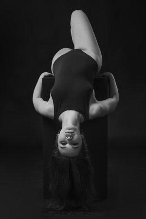 Pretty brunette woman in bodysuit posing on cube on black background. Black and whiteの写真素材