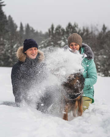Cute young couple having fun with their dog in winter forestの写真素材