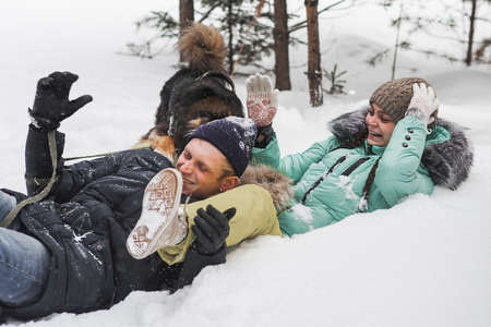 Cute young couple having fun with their dog in winter forestの写真素材