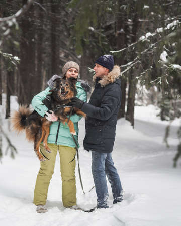 Cute young couple walking and having fun with their dog in winter forestの写真素材