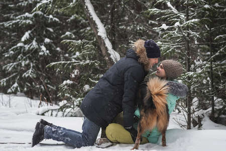 Couple in love having fun with dog in the snow in winter forestの写真素材