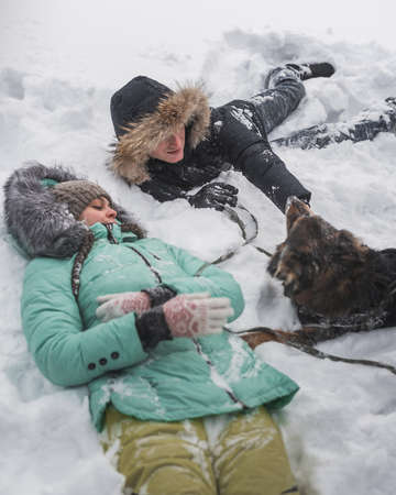 Couple in love having fun with dog in the snow in winter forestの写真素材