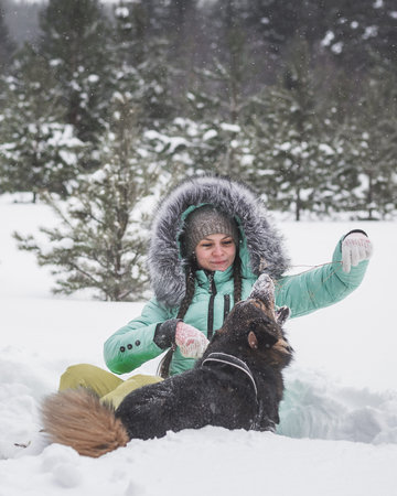 Woman having fun with dog in the snow in winter forestの写真素材