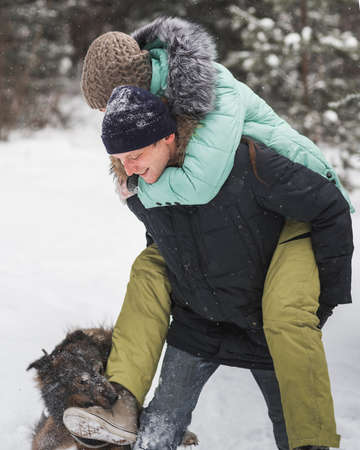 Happy young couple. Man piggybacking his girlfriend in winter forestの写真素材