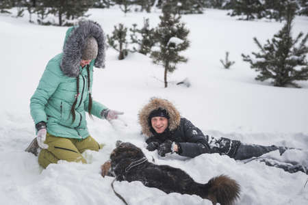 Couple in love having fun with dog in the snow in winter forestの写真素材