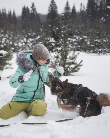 Woman having fun with dog in the snow in winter forestの写真素材