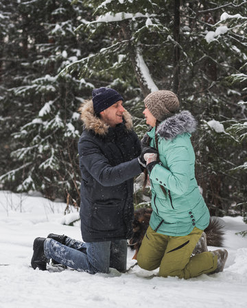 Couple in love having fun with dog in the snow in winter forestの写真素材