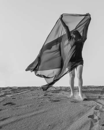Woman in black with flying fabric dancing on the sand dune. black and whiteの写真素材